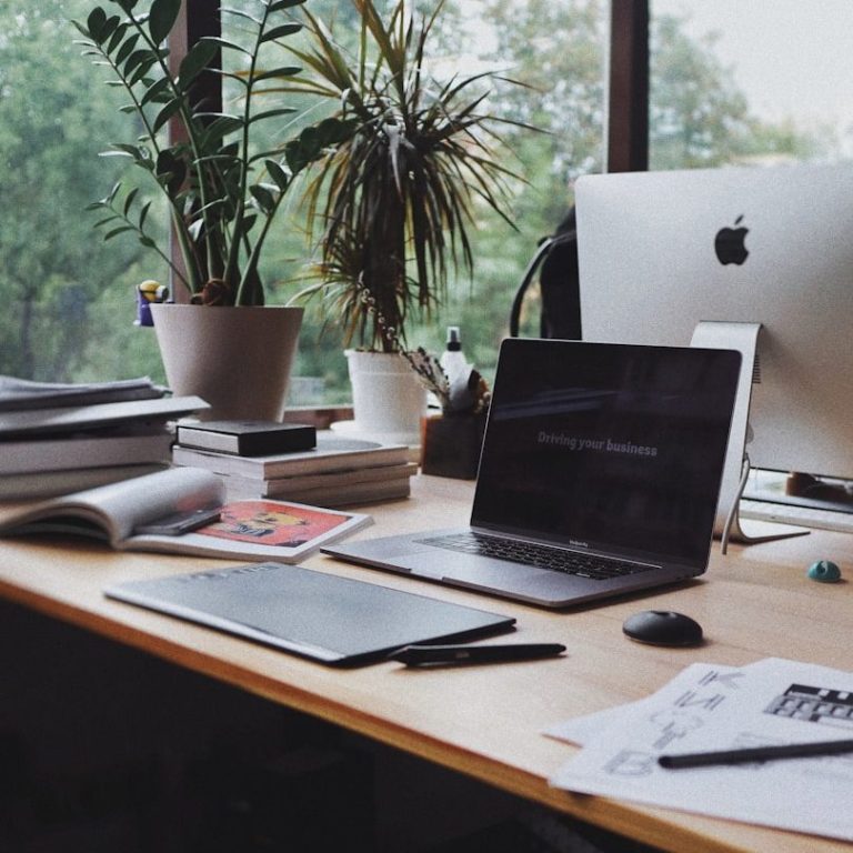 Backoffice Ein moderner Schreibtisch mit Laptop, Notizblöcken und Pflanzen im Hintergrund.